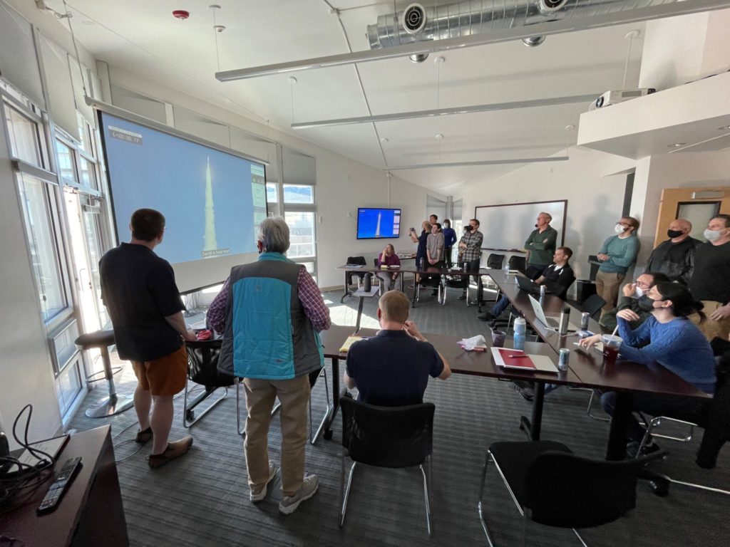 Researchers standing in a room looking at a live image of the GOES-T satellite launch.