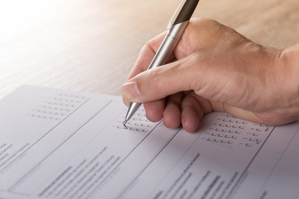 A person's hand holding a pen and filling out a survey.