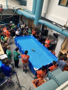 High-angle view of a model submarine in a test tank as students and camp leaders look on.