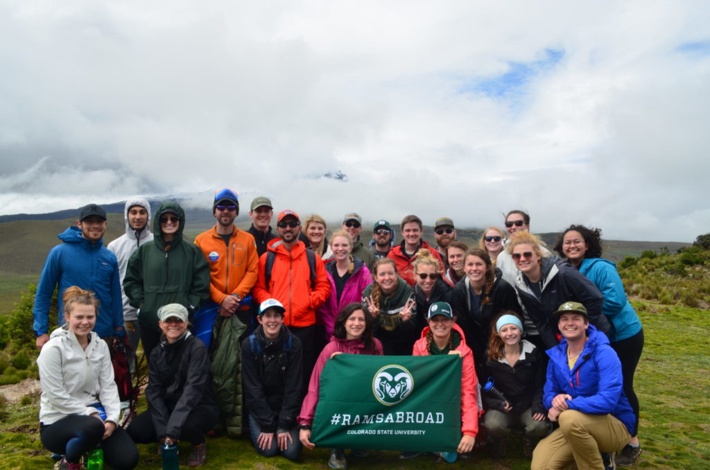 A group of students on a hike pose for a group portrait while displaying a flag with CSU Ram logo and the words "Study Abroad"