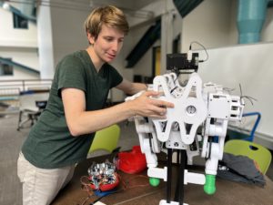 A student works with a large white robot on a tabletop