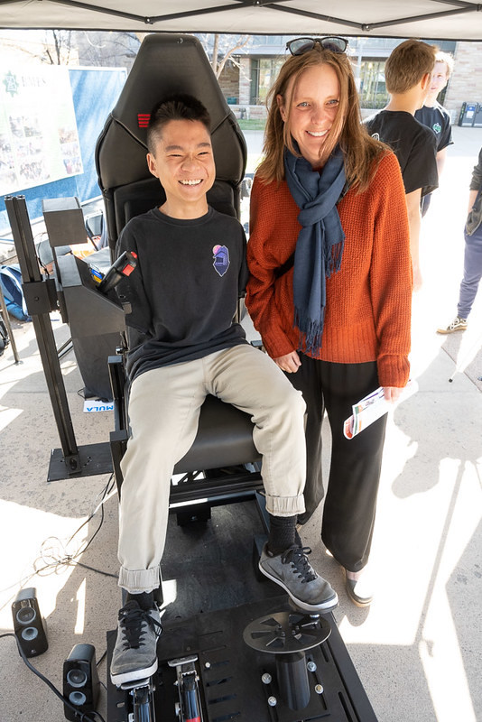 A picture of Jian Cohen, business student, testing out a driving simulator next to Heather Zoccali, a family friend, on the LSC plaza, April 24, 2023 on E-Days.