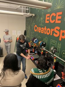 Elementary school students observe as an engineering student demonstrates how to use a 3D printer in front of the ECE CreatorSpace sign.