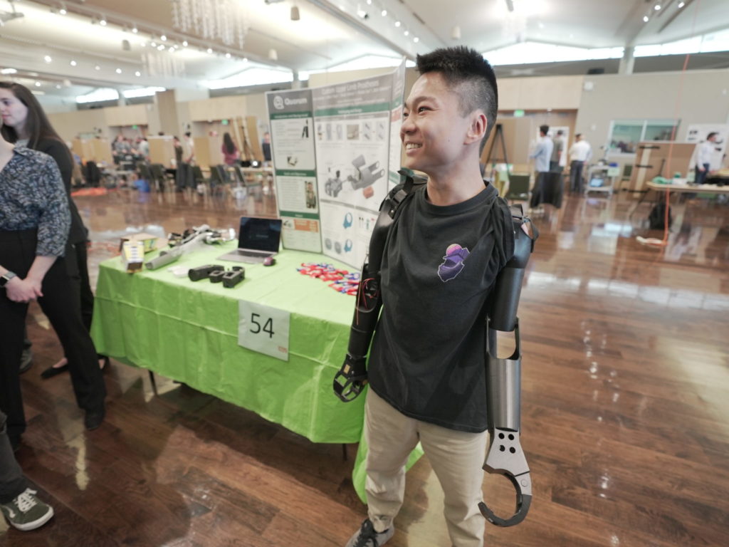 A photo of business student Jian Cohen showing off his prosthetic arms developed by biomedical engineering students at E-Days.
