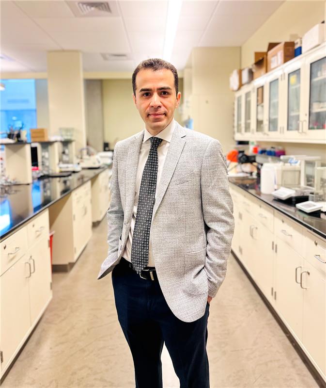 Yourdkhani, wearing a jacket and tie, gazes into the camera in a brightly lit laboratory setting