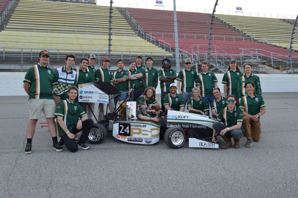 A picture of the Ram Racing team surrounding their car inside a race track.