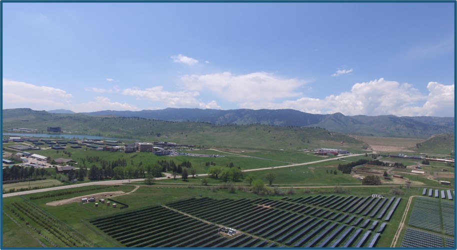 An array of solar panels in the foreground, with the foothills of the Rockies in the background.