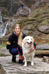 Mastrocola, in civilian clothes, poses in front of a waterfall with her dog.