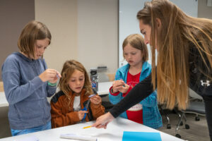 Photo showing a college student working with elementary school students on a craft project.