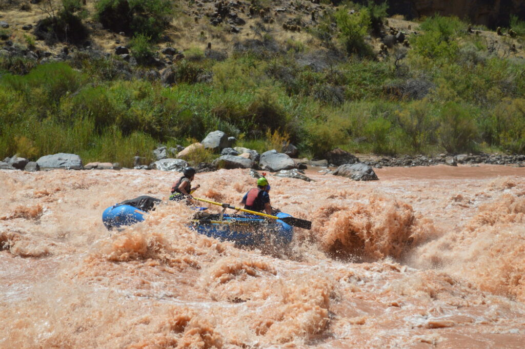 A blue inflatable raft in the midst of turbulent brown water at the bottom of the Grand Canyon