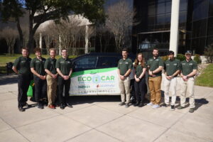 Nine CSU engineering students - eight men and one woman – stand in front of a car with “EcoCAR” written on the door. 