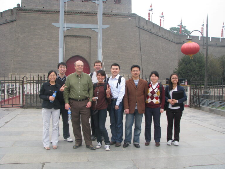 Collett poses with a group of students in China. In the background, an Asian paper lantern and other elements of Chinese architecture.