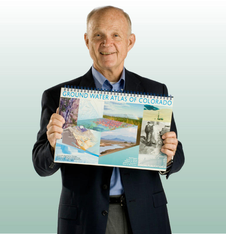 A studio portrait of Neil Grigg holding a copy of a large-format, spiral-bound book titled, “Ground Water Atlas of Colorado”